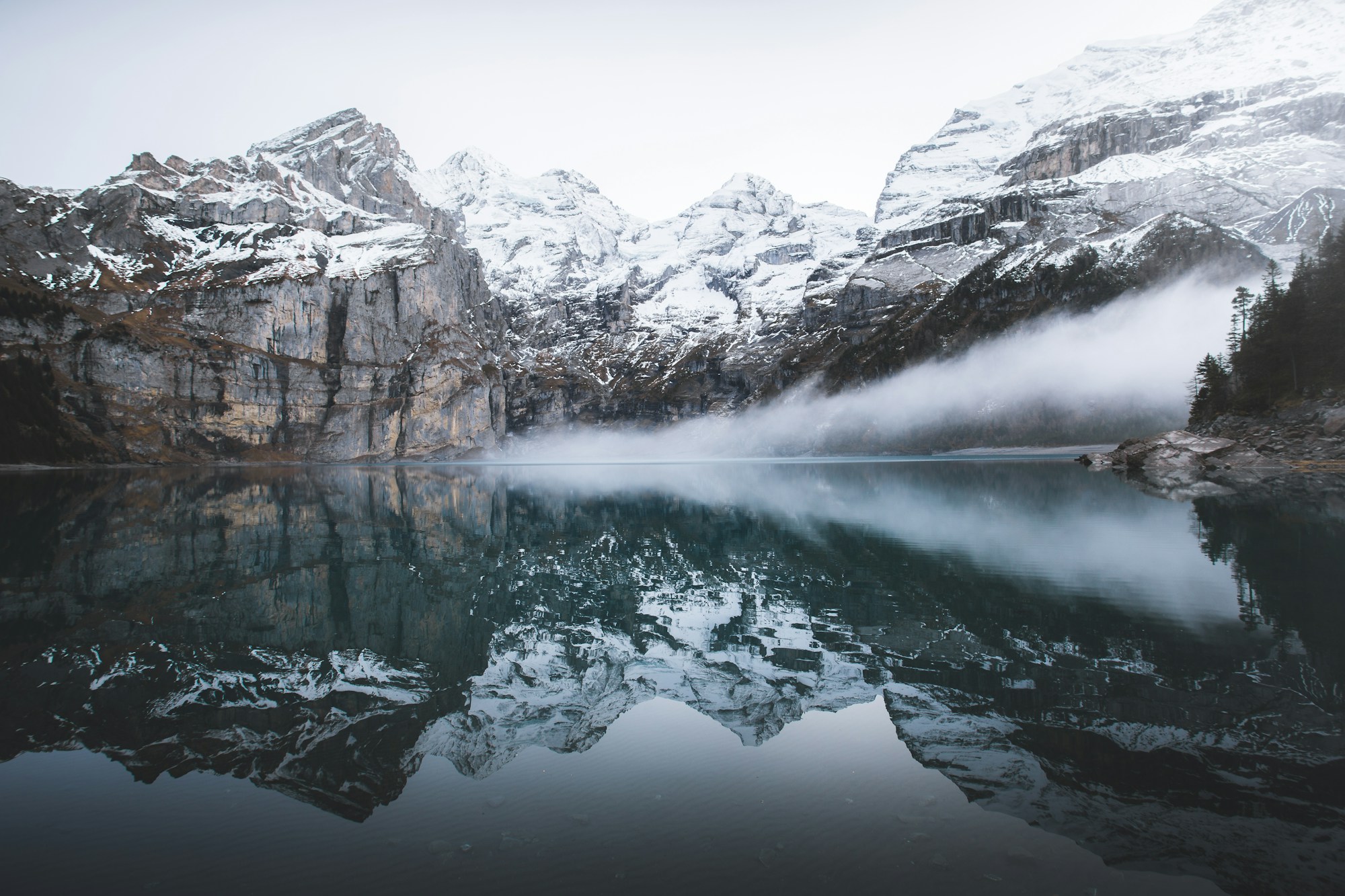 Snow-covered mountain faces and mist reflected in an alpine lake